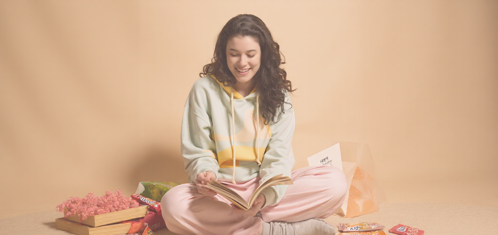 Woman sitting on the floor with a book and candy, against a beige background