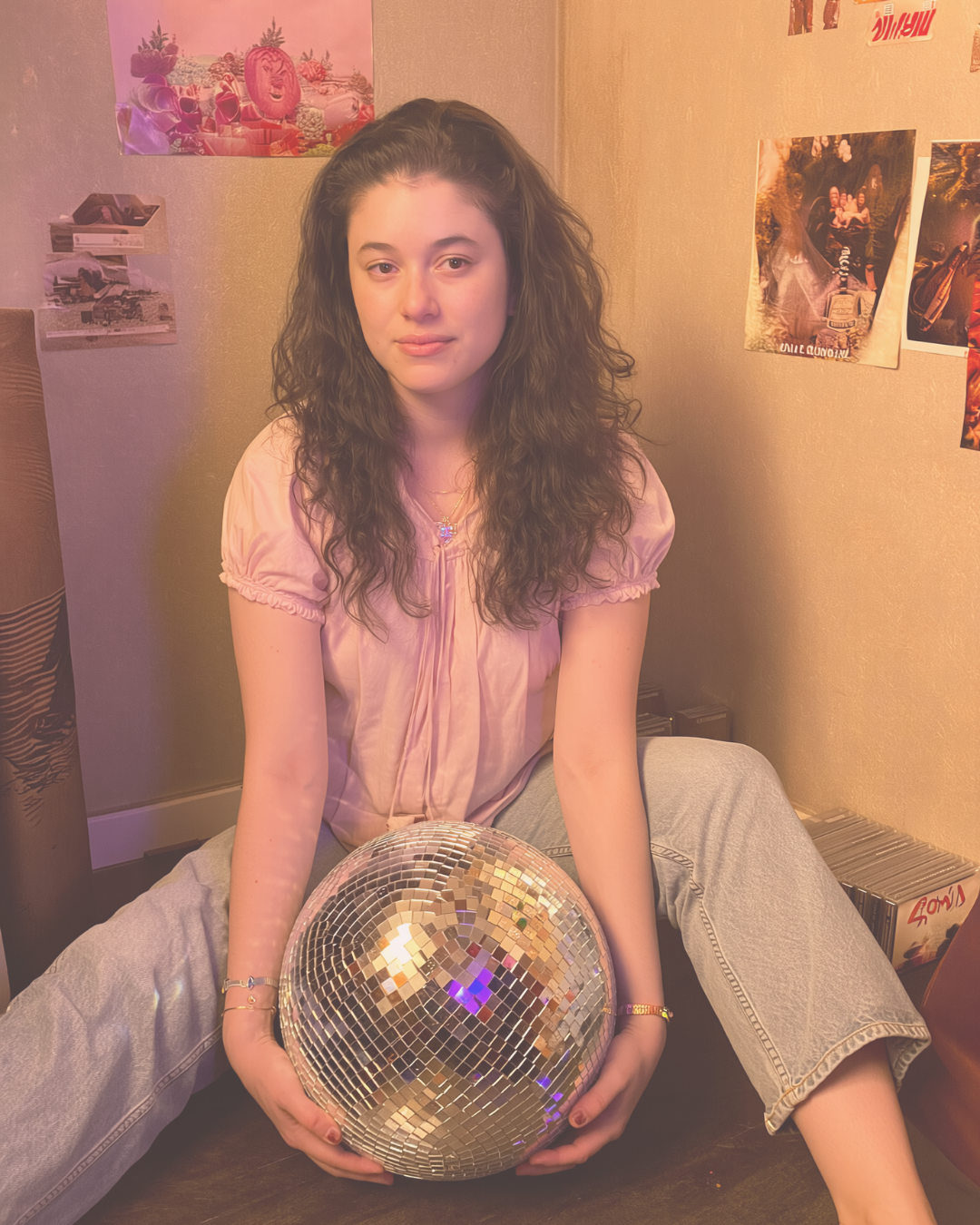 Person holding a disco ball in a room with posters on the wall